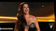 a woman in a black strapless dress is laughing in front of a screen that says en vivo