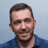 a man with a beard wearing a blue shirt smiles
