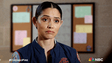 a woman in a chicago fire uniform looks sad in front of a bulletin board