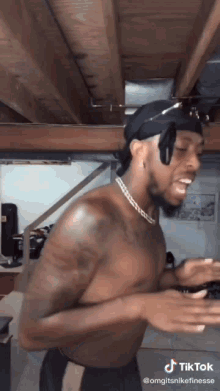 a shirtless man wearing a headband and a necklace is dancing on a tiktok video