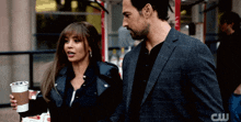 a man in a suit and a woman in a leather jacket are standing next to each other with the letters cw visible