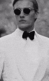 a man in a white tuxedo and bow tie is wearing sunglasses and a bow tie .