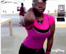 a woman wearing glasses and a pink shirt is standing in a room .
