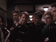 a group of young men are standing in a dark hallway and one of them is holding a saxophone and wearing glasses