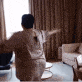 a woman is dancing in a living room with her arms outstretched .