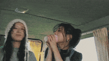 two women in a car one wearing a knitted hat drinking from a cup