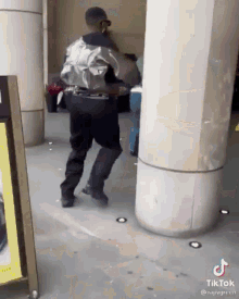 a man in a silver jacket and black pants is dancing in front of a sign that says tiktok .