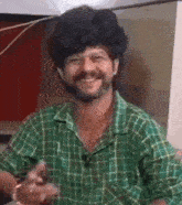 a man with a beard is wearing a green plaid shirt and smiling at the camera .