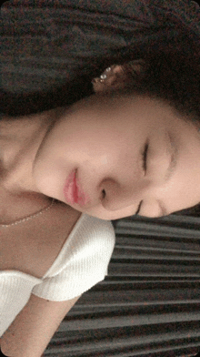 a woman laying down with her eyes closed wearing a white shirt