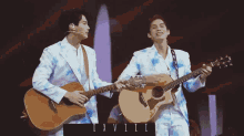 two men are holding guitars on a stage and one of them is wearing a tie dye suit