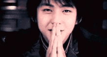 a close up of a young man with his hands folded in front of his face .