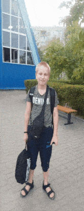 a boy wearing a shirt that says deni o. stands in front of a blue building