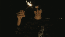a woman wearing sunglasses holds a sparkler in front of her face