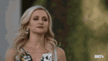 a woman in a floral dress is standing in front of a building and looking at the camera .