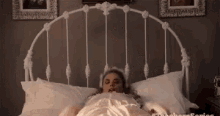 a woman is laying in a bed with a white headboard and pillows .