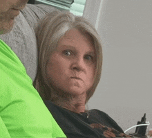 a woman sits on a couch with a man in a green shirt behind her