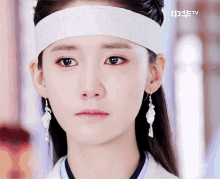 a close up of a woman wearing a headband and earrings with a tv logo behind her
