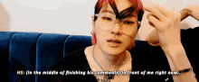 a man with pink hair and glasses is sitting on a blue couch and talking to someone .