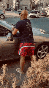 a man wearing a shirt that says " enjoy your life " is standing next to a car