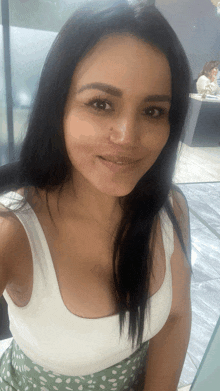 a woman wearing a white tank top and a green skirt smiles for the camera