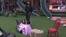 a woman in a purple dress is sitting on a bean bag chair while a man stands next to her .