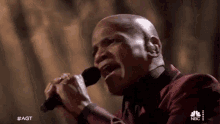 a man in a red suit is singing into a microphone on a stage .