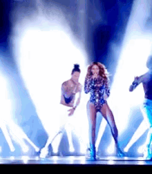 a woman singing into a microphone on a stage with a man dancing behind her