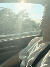 a man sitting in a car looking out the window with the sun shining through the trees