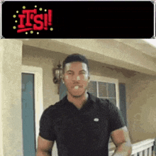 a man in a black shirt is standing in front of a house and a sign that says it 's !
