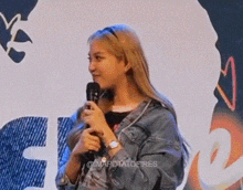 a woman in a denim jacket is standing in front of a microphone and smiling .