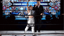 a man in a suit stands next to a woman in a wrestling ring in front of a stardom awards sign