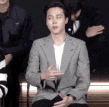 a man in a suit is sitting in front of a group of people and making a funny face .