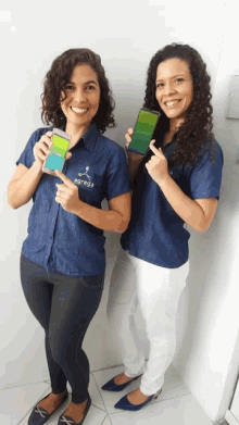 two women standing next to each other holding up their phones one of which says agrega