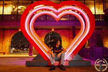 a man in a supreme shirt sits in front of a large heart