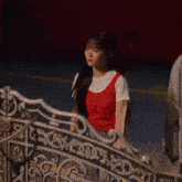 a woman in a red top is standing in front of a wrought iron gate