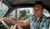 a man wearing sunglasses and a plaid shirt driving a car