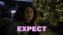 a woman stands in front of a sign that says expect shagarita