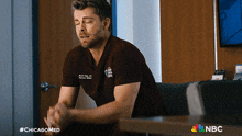 a man in a scrub is sitting at a table with the nbc logo on the bottom