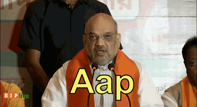 a man with a beard and glasses stands in front of a microphone and says aap