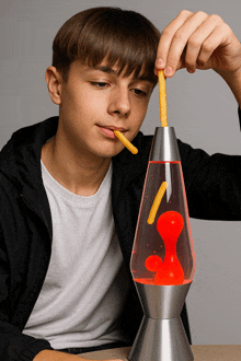 a young boy is playing with a lava lamp and eating french fries out of it