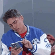a young man in a blue jacket is holding a cell phone .