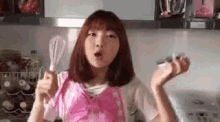 a woman in a pink apron is holding a whisk and a spoon .