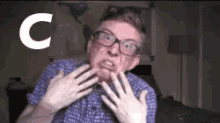 a man wearing glasses and a plaid shirt is making a funny face with the letter c behind him .