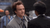 a man in a trench coat and tie is talking to another man in a suit