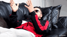a man wearing sunglasses and a red and black jacket is laying on a couch