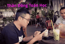 a man sits at a table looking at his cell phone with the words than dong toan hoc written above him