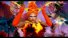 a drag queen with orange hair and red gloves is wearing a carnival mask