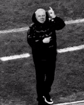 a man in a hooded jacket is standing on a field and giving the middle finger .