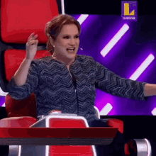 a woman is sitting in a chair with her arms outstretched in front of a television screen that says latina on it .