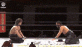 two men are wrestling in a ring and one of them is kneeling down on the ground .